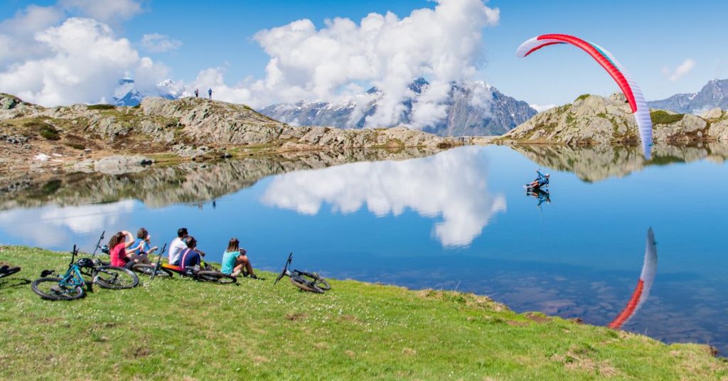 Groupe de VTT assis devant un lac de montagne sur lequel se pose un parapente